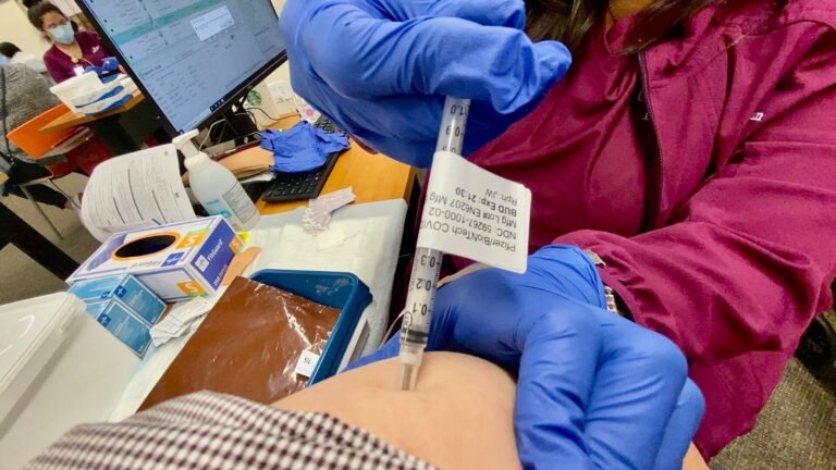 A gloved healthcare worker preparing a vaccine syringe